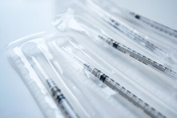 Closeup disposable syringes with needle for medical purpose and COVID-19 in a clear plastic package on white table background at clinic or hospital. Healthcare and vaccination concept