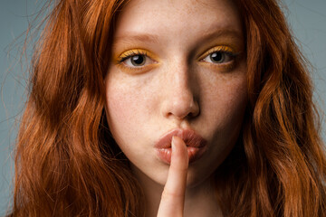 Young ginger woman with makeup showing silence gesture at camera