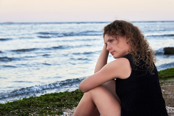 Fototapeta na wymiar A thoughtful woman sits alone on the sea beach near the water.