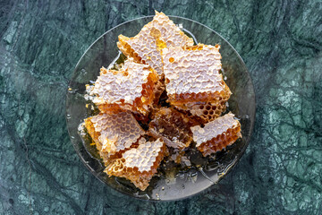 Several sliced pieces of honeycomb filled with fresh, golden honey lie on a plate. Top view.