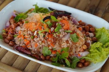 Mixed salad with pork and dried shrimp, vegetables placed on a white plate on a bamboo floor.