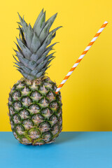 Pineapple with straw on yellow and blue background. Fresh juice creative concept.