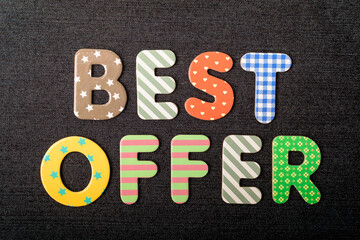 Card with Best Offer words made from mixed vivid colored wooden letters on a textured dark black textile material that can be used as a message.