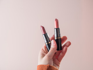 Obraz premium What lipstick should I use for my lips today? She holds open lipsticks in her hand. Powdery background
