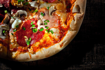 Round pizza on a wooden board. Pizza on a black table close up. Contrasting dramatic light as an artistic effect.