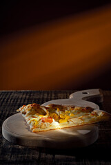 Triangular slice of pizza on a wooden board. Pizza on orange background close up. Copy space and free space for text near food.