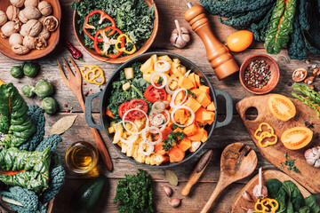 Pot with sliced colorful vegetables and cooking utensils on rustic wooden background. Top view....