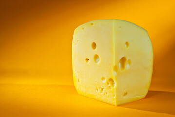 Yellow piece of cheese on an orange background. Triangular cheese close up. Copy space and free space for text near the cheese.