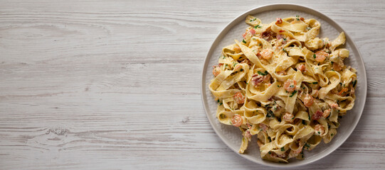 Homemade Garlic Shrimp Bacon Alfredo on a plate on a white wooden background, top view. Flat lay, overhead, from above. Space for text.