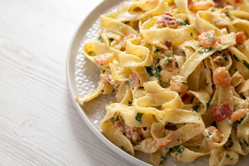 Homemade Garlic Shrimp Bacon Alfredo on a plate on a white wooden background, low angle view. Copy space.