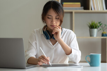Shot of asian woman working with a stylus pen on a digital tablet and laptop computer at home....