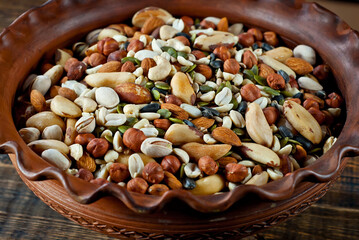 Many types of nuts close up. Texture of different nuts on a wooden board. Clay bowl on a brown table.