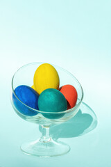 Hand-painted colorful Easter eggs in a transparent glass vase on a light blue background, vertical frame, copy space