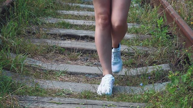 Female feet in sneakers walking along old abandoned and overgrown railway, summer light day