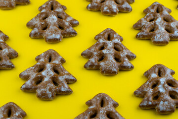 Christmas tree cookies on yellow background. New Year's food. Festive baked goods. Gingerbread on the table. Icing sugar sweetness taste season. Pattern