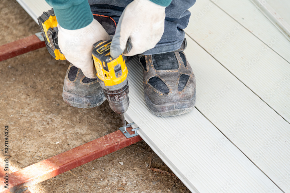 Wall mural man assembling composite deck using cordless screwdriver.