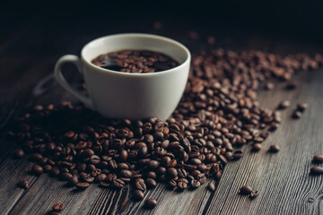 coffee beans scattered on a wooden table and a cup with a hot drink aroma