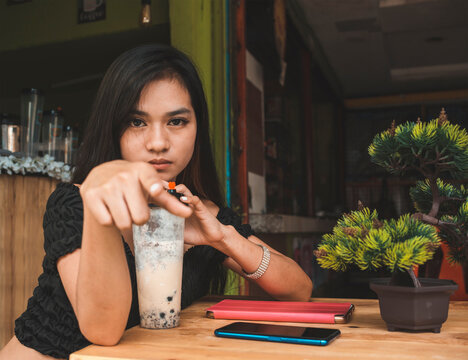 An upset young asian woman points at someone with a condescending look, while at a cafe sipping on milk tea.