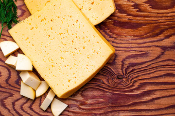 two large pieces of cheese on a wooden table surrounded by herbs and small pieces of cheese copyspace