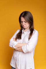 Portrait of frowning beautiful girl in white blouse, arms crossed on chest, on yellow isolated background