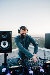 Professional Disco DJ in face mask mixing songs with his mixer board, playing music at a terrace...