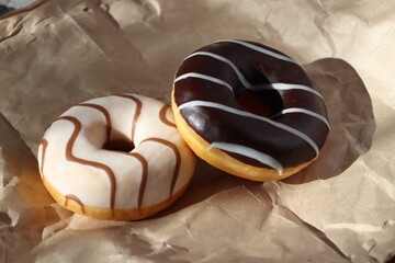 Two donuts with caramel and chocolate frosting on brown paper with shadows