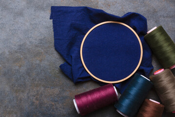 Top view of embroidery hoops, blue fabric and dark green,blue vonius, brown threads on the rural...