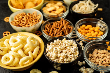 Assorted chips, popcorn, onion rings, croutons, cheese balls, biscuits in bowls. unhealthy food for figure, heart, skin, teeth. An assortment of fast carbohydrates. Junk food on a stone background