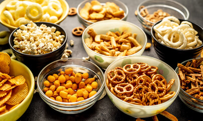 Assorted chips, popcorn, onion rings, croutons, cheese balls, biscuits in bowls. unhealthy food for figure, heart, skin, teeth. An assortment of fast carbohydrates. Junk food on a stone background