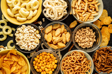 Assorted chips, popcorn, onion rings, croutons, cheese balls, biscuits in bowls. unhealthy food for figure, heart, skin, teeth. An assortment of fast carbohydrates. Junk food on a stone background