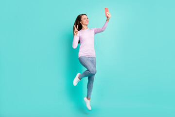 Full length body size view of beautiful cheerful girl jumping taking selfie showing v-sign isolated over turquoise bright color background