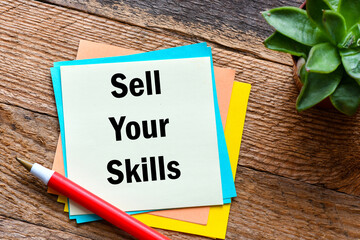 SELL YOUR SKILLS words written on a small piece of paper and a wooden table.