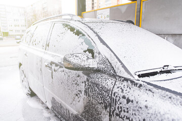Car covered with washing foam at contactless car washing service