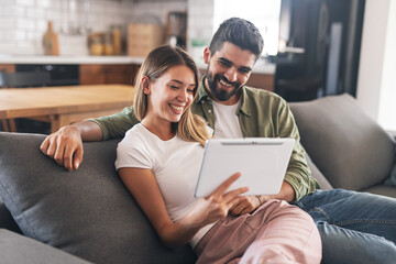 Excited modern couple smiling while looking at tablet