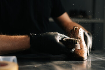 Close-up hands of shoemaker wearing black gloves swipes dust off the shoe brush in dark craft shoe...
