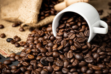 Coffee beans roasted in a white cup with were placed on a sackcloth on a black stone floor.
