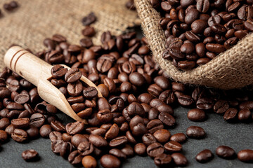 Coffee beans roasted in sackcloth with a wooden scoop on a black stone floor.