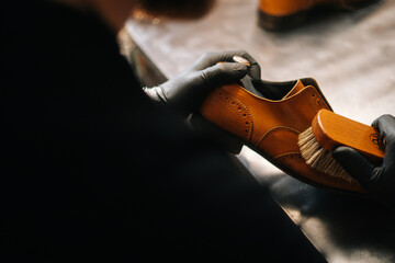 Close-up back view of unrecognizable shoemaker cleaning with brush old light brown leather shoe....