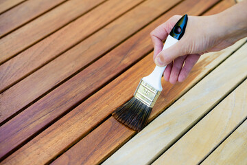 hand holding a brush applying varnish paint on a wooden garden table - painting and caring for wood with oil - 421203811