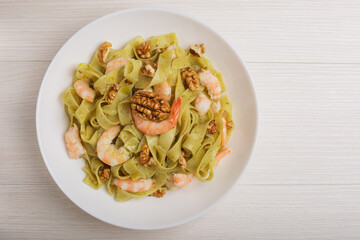 The Italian pasta with shrimp, pesto sauce, walnut on white plate on wooden table. Top view. Mediterranean cuisine.
