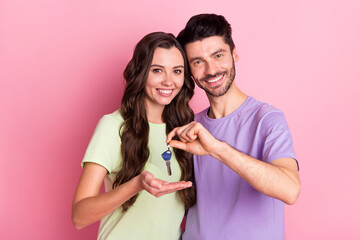 Portrait of attractive cheerful couple embracing holding in hand key home credit loan invest isolated on pink pastel color background