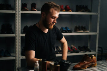 Portrait of handsome bearded shoemaker examining light brown leather shoes during restoration working, looking at camera. Concept of cobbler artisan repairing and restoration work in shoe repair shop. - Powered by Adobe