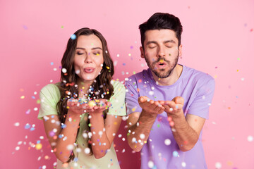 Portrait of attractive dreamy cheerful couple blowing decorative elements isolated over pink pastel...