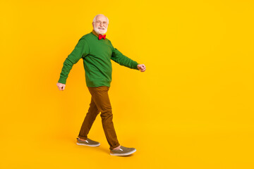 Full length photo of funny sweet mature man dressed pullover bow tie glasses walking empty space isolated yellow color background
