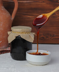 molasses in glass bowl and in wooden spoon  - 421208298