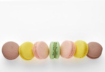 Horizontal photo of macaroon. Colorful cakes macaron with pastel tones laid out in a strip on white background. Free space on the top for your text. Top view of almond cookies.
