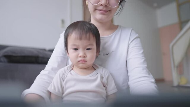 Adorable cute baby sit on mother lap watching still on tablet screen with black hair mother at home, Coronavirus COVID-19 quarantine, distance education online learning lesson concept, stay safe home