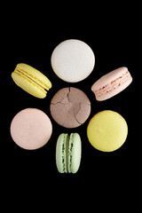 Macaroon. Six colorful cake macaron with pastel tones and one cracked lay and stand in the shape of a flower on black background. Top view of almond cookies.