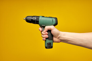 Battery screwdriver or drill in hands isolated over yellow background