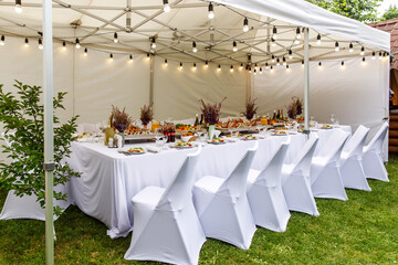 Wedding white tent with white chairs. Banquet hall under a tent for wedding or another catered...